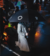 Person holding a black umbrella with visible branding on a rainy street.